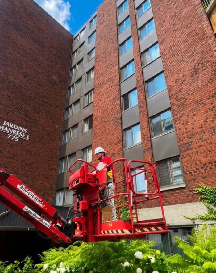 Technicien casqué en nacelle devant un immeuble à condos